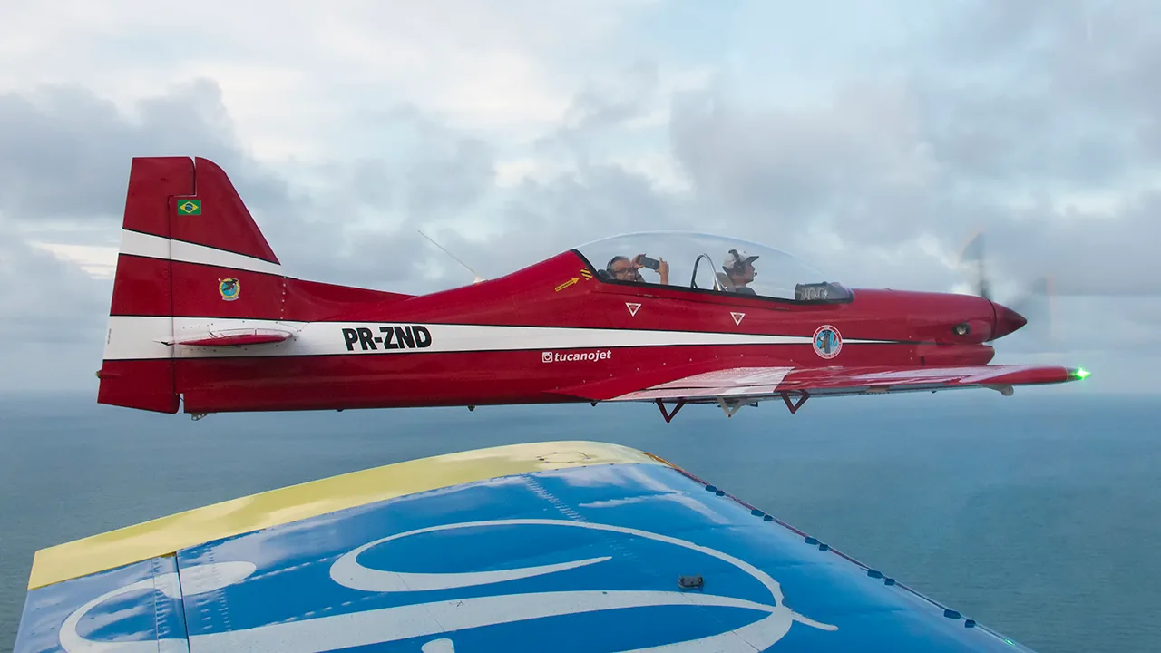 The red Tucano replica PR-ZND in flight over the sea, seen from a formation aircraft