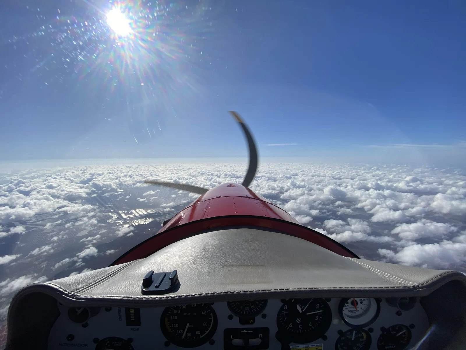 View from the cockpit over the nose and propeller, above a layer of clouds